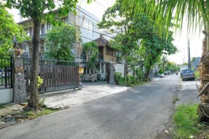 A residential street with a gated entrance, a parked car, and a building with a traditional roof. - Urbanview Hotel Wayan Mansion (Bali)
