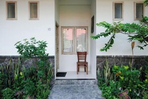 A doorway with a chair, a stone step, and a white wall with windows. - Urbanview Hotel Wayan Mansion (Bali)