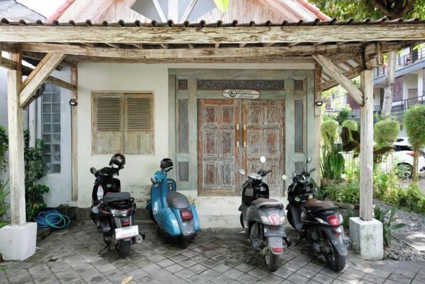 Un porche abrité où sont garés trois scooters, devant un immeuble doté d’une porte et de fenêtres de style traditionnel.