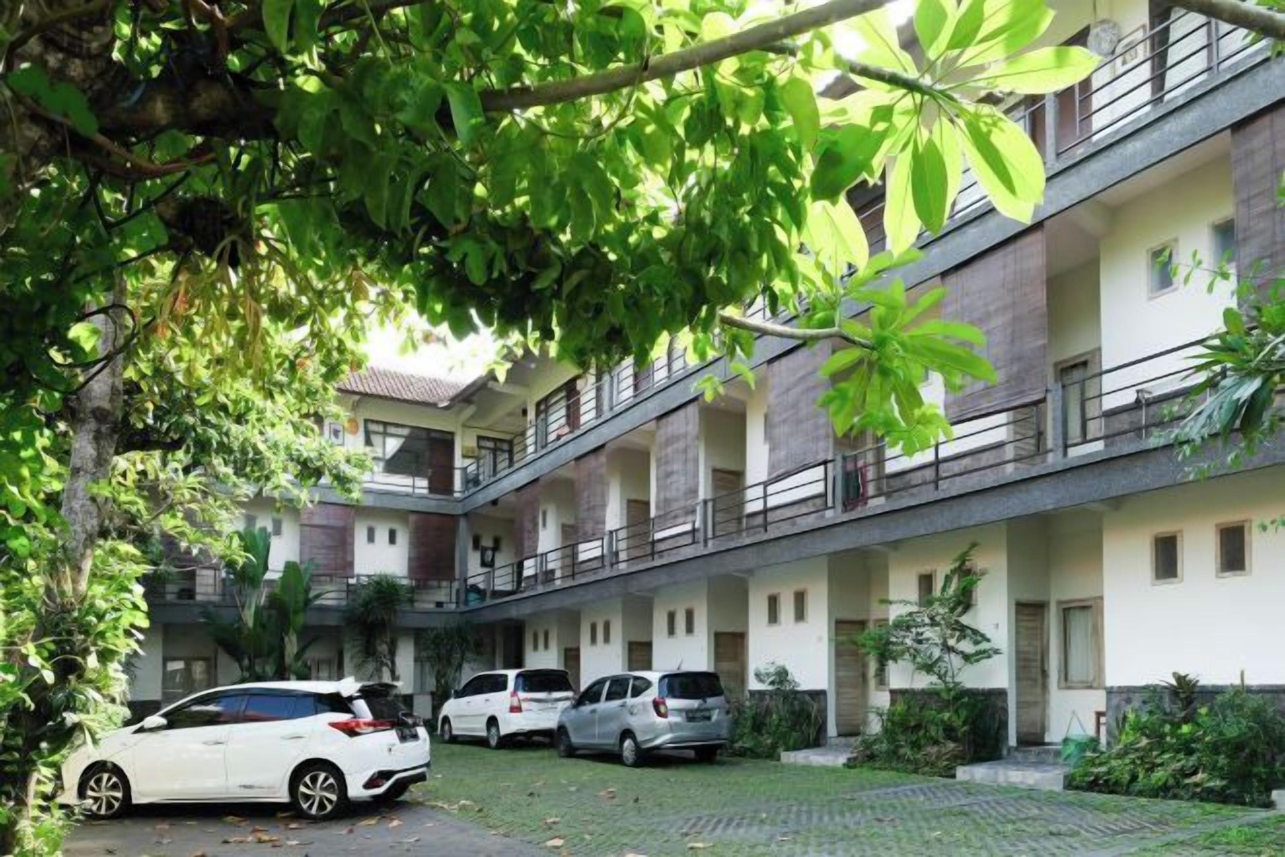 A multi-story building with a courtyard, several parked cars, and lush greenery.