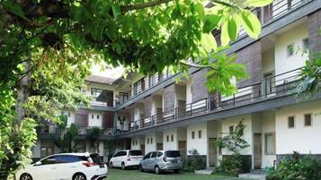 A multi-story building with a courtyard, several parked cars, and lush greenery.