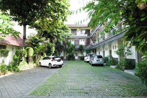 Une cour où sont garées des voitures et un immeuble à plusieurs étages doté de balcons.