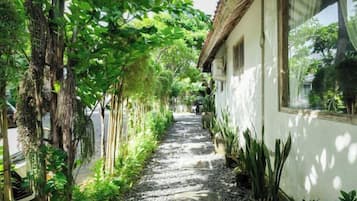 A narrow pathway flanked by greenery and a building with a sloped roof.