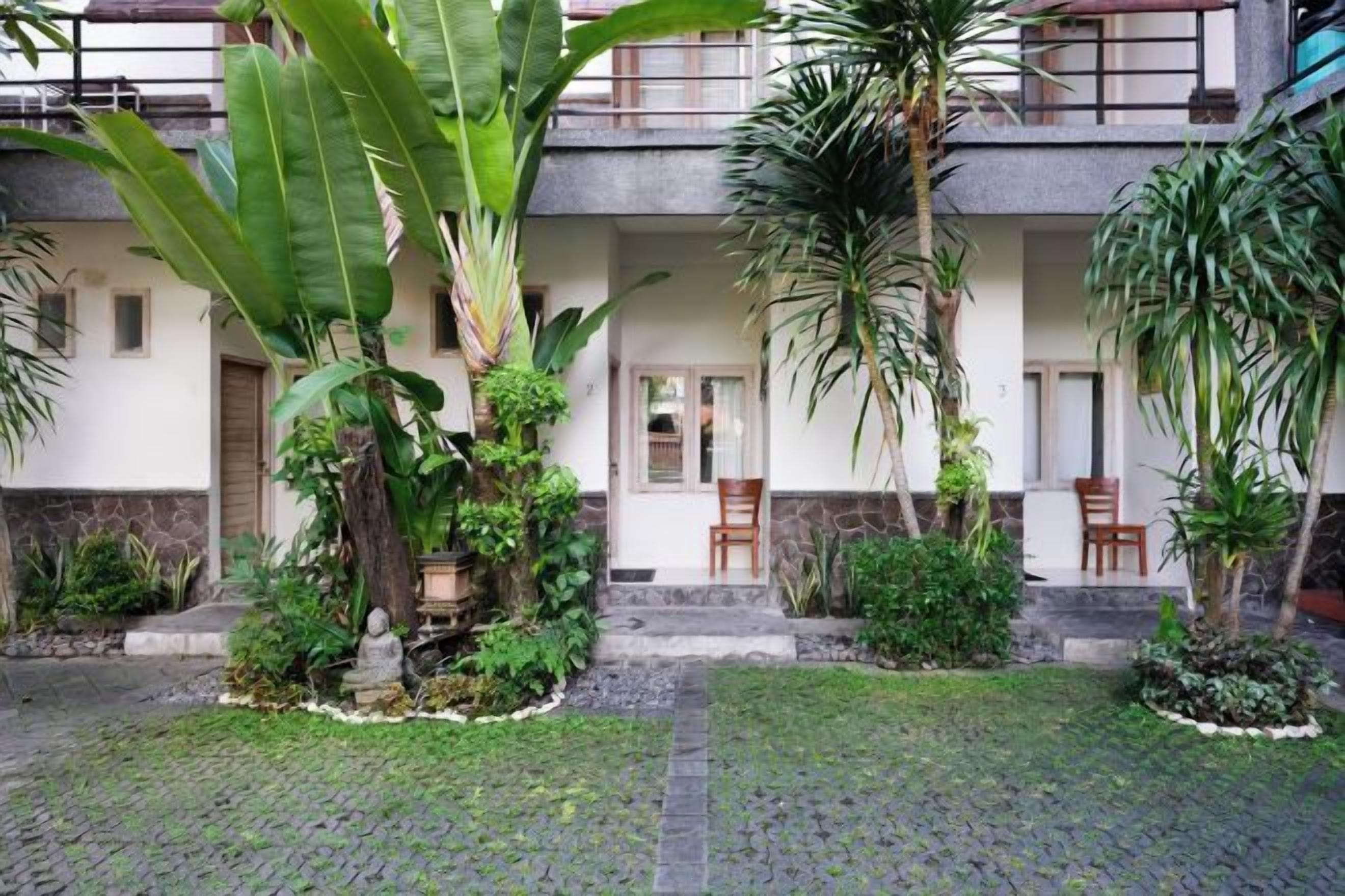 A courtyard with a paved walkway, potted plants, and a seating area with chairs.