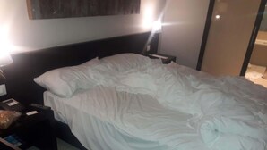 A neatly made bed in a hotel room with a headboard, a bedside table with a remote control, and a nightstand with a lamp. - Potchefstroom Guest House with WiFi (Potchefstroom)