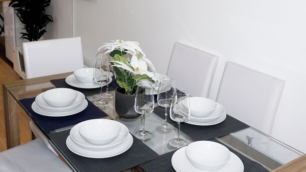 A dining table set with white plates, bowls, and wine glasses, accompanied by a potted plant. - Biz & Fam Sleeps 7 Wigan w/ Parking, Self-check-in (Wigan)