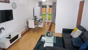 A living room with a black leather sofa, a glass coffee table, and a dining area with a white table and chairs. - Biz & Fam Sleeps 7 Wigan w/ Parking, Self-check-in (Wigan)