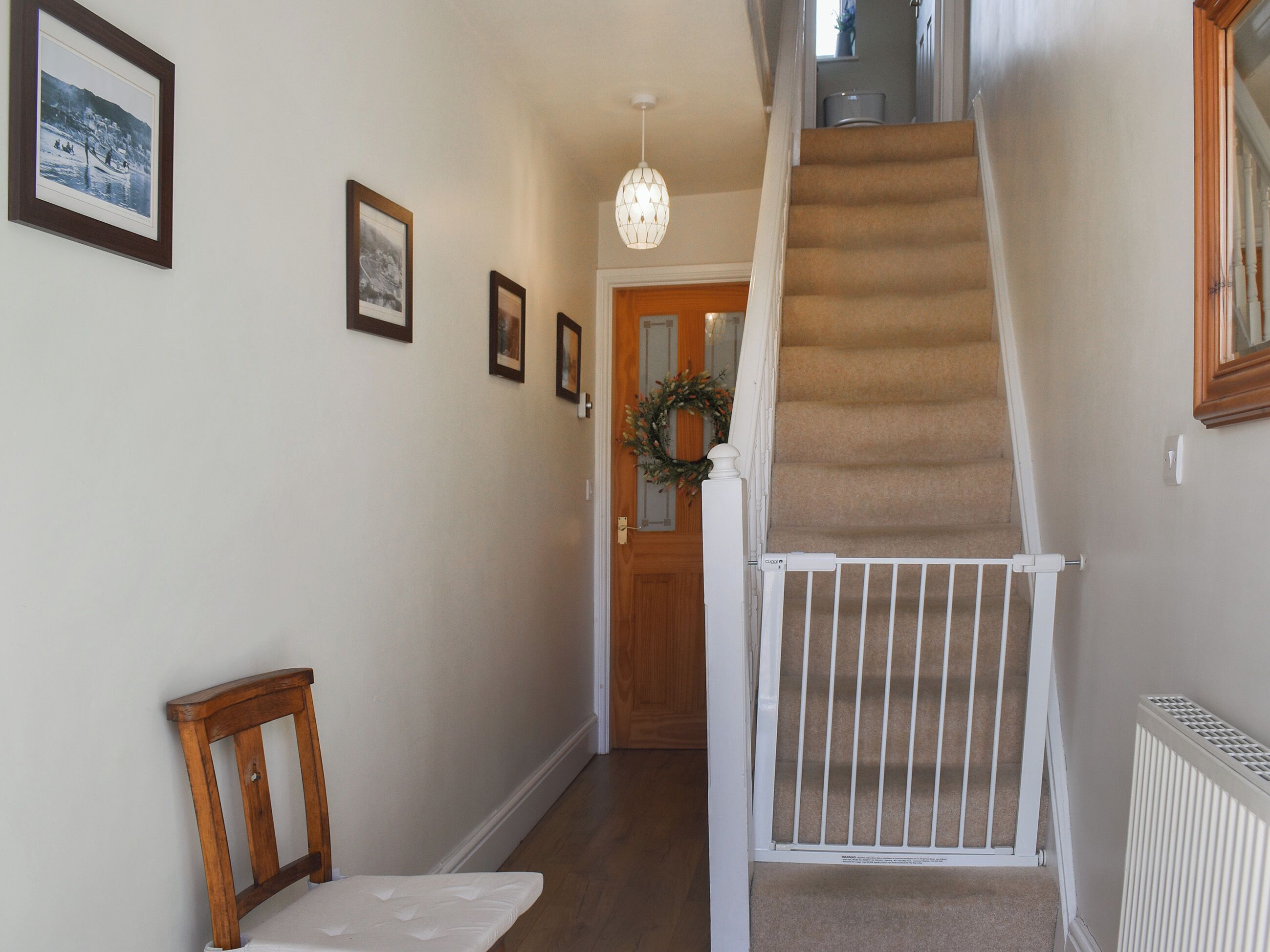 A hallway with a staircase, a wooden chair, a white bench, and framed pictures on the wall.