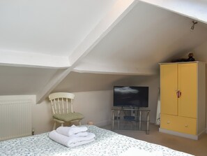 Ein Schlafzimmer mit einem Bett, einem Fernseher auf einem Schrank, einem gelben Kleiderschrank und einer weißen Heizung.