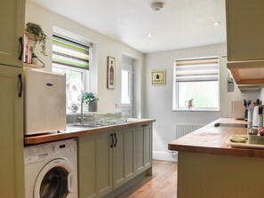 A kitchen with a built-in washing machine, a sink, and a window with blinds.