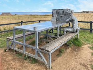 Ein Metall-Picknicktisch mit Bänken, vor einer ländlichen Kulisse mit freiem Blick auf das Meer.