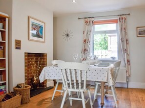 A dining area with a table set for four, white chairs, a fireplace, and a window with curtains.