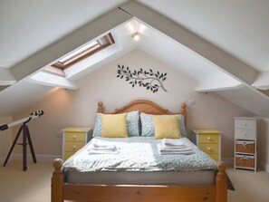 A bedroom with a sloped ceiling, a bed with a wooden headboard, two bedside tables, a wall-mounted decoration, and a telescope on a tripod.