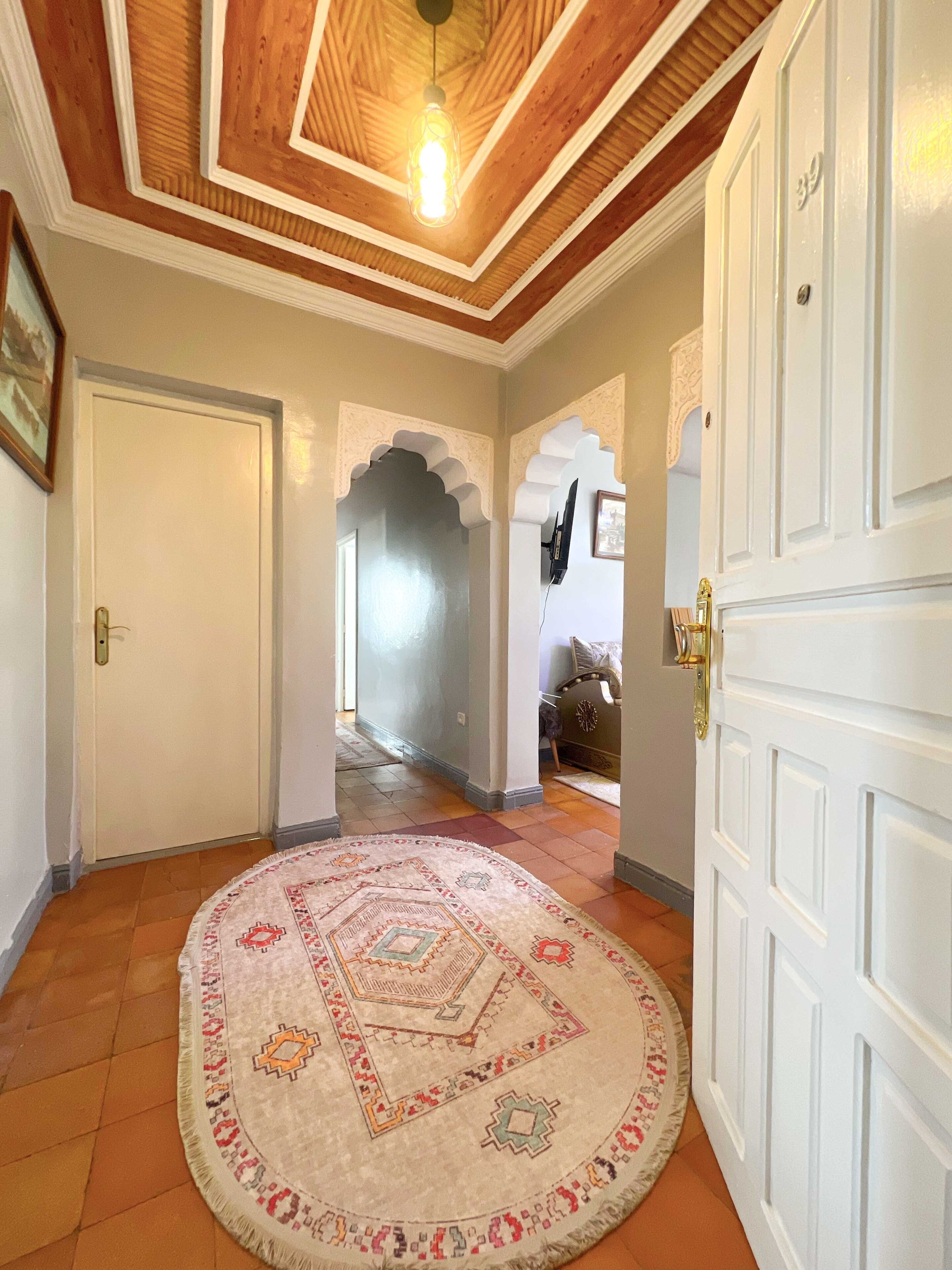 A hallway with a round patterned rug, white doors, and a wooden ceiling with a hanging light fixture.