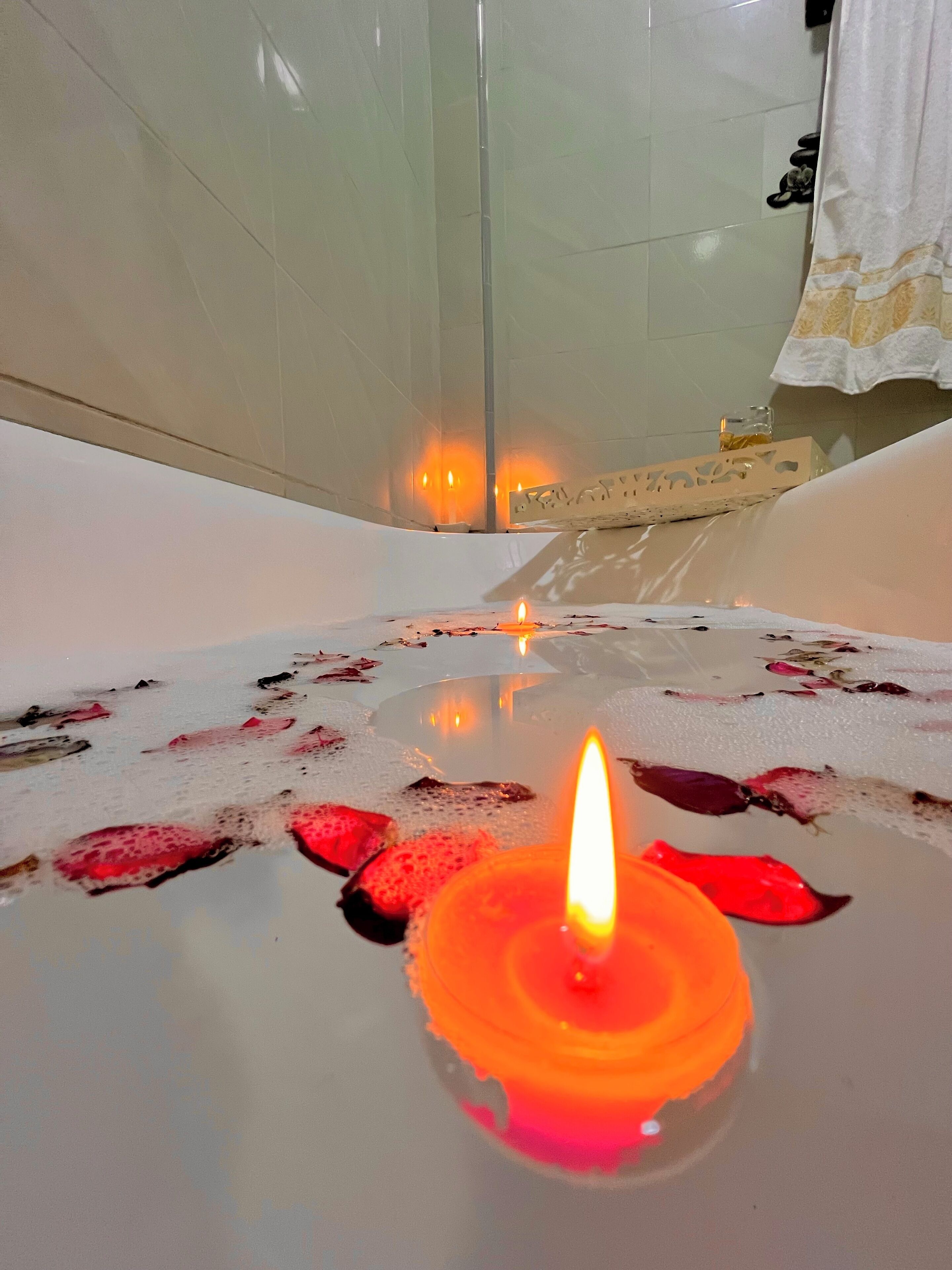 Eine Badewanne mit einer brennenden Kerze, Rosenblüten und einem Handtuchhalter im Hintergrund.