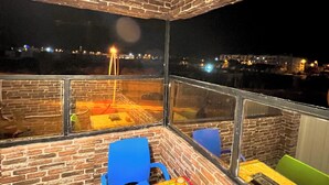 Una habitación de esquina con paredes de ladrillo, una mesa con mantel amarillo y vistas a una obra en construcción.