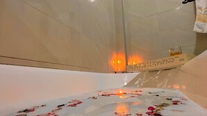 Una bañera con pétalos de rosa y velas, un perchero y una pared decorativa.