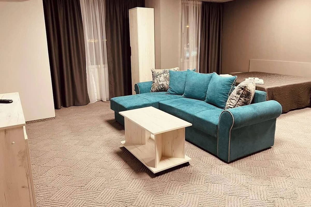 A modern living room with a teal sofa, a white coffee table, and a large window with sheer curtains.