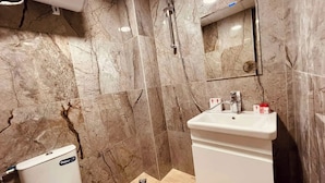 Un baño con paredes de mármol, inodoro, lavamanos y ducha.