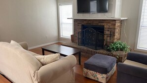 Una sala de estar con chimenea, un sofá, un reposapiés y un televisor sobre la chimenea.