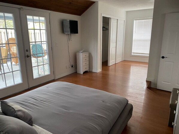 Une chambre à coucher avec un grand lit, une commode, un téléviseur fixé au mur et une porte donnant sur une salle de bain.