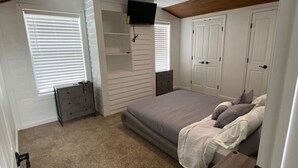 Un dormitorio con cama, cómoda, televisor montado en la pared y armario.