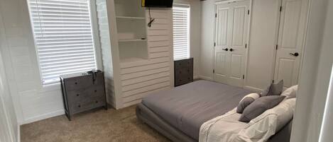 A bedroom with a bed, a dresser, a TV mounted on the wall, and a closet.