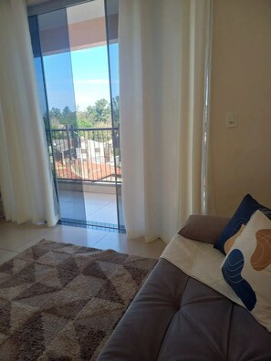 Ein Wohnzimmer mit einer Couch, einem gemusterten Teppich und Blick durch eine Glastür auf einen Außenbereich mit Geländer.