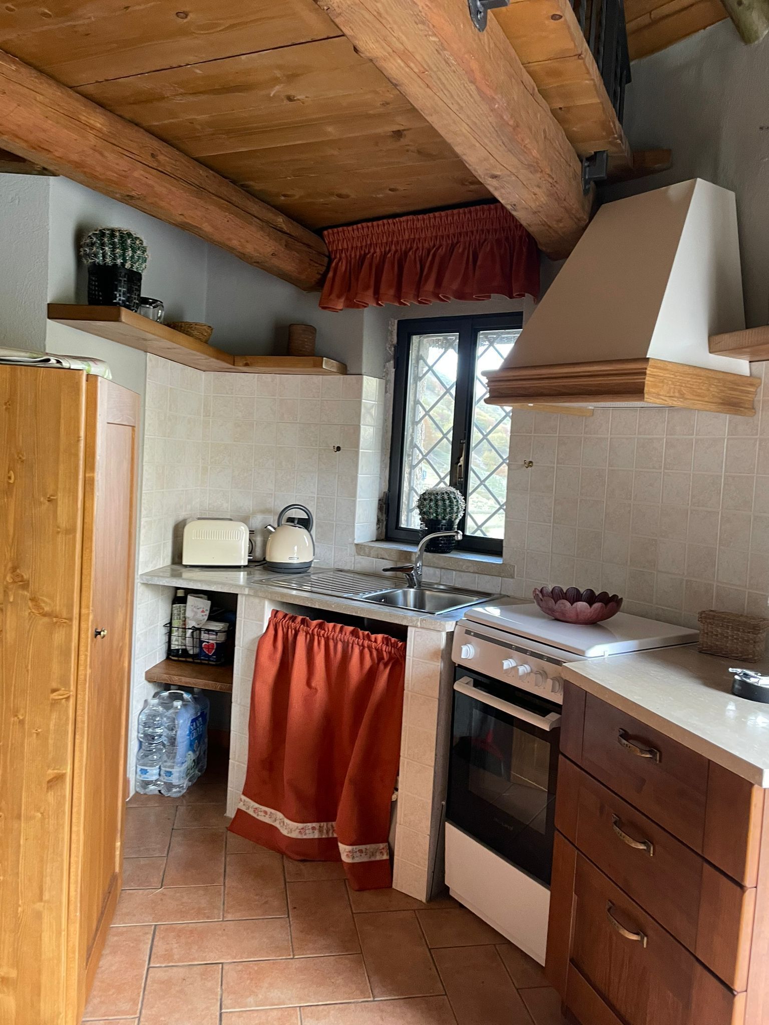 Une cuisine compacte avec des poutres en bois, une fenêtre offrant une belle vue, une bouilloire et un évier.