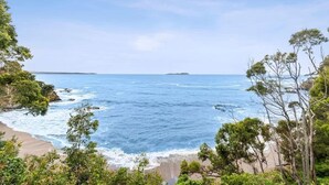 A coastal landscape with a beach, ocean, and surrounding greenery. - Tollgate Beach House (Denhams Beach)