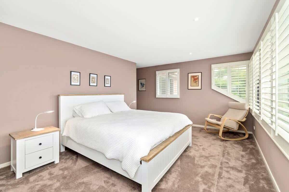 A bedroom with a bed, bedside table, chair, window, and wall art.
