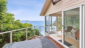 A balcony with a view of the ocean, a glass door leading to a room with a chair and a table, and a wooden deck. - Tollgate Beach House (Denhams Beach)