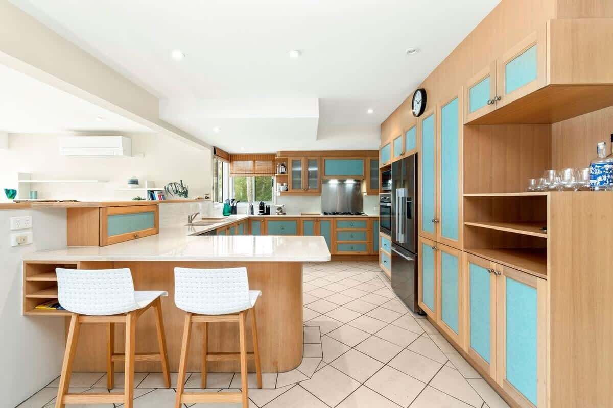 A modern kitchen with a central island, bar stools, wooden cabinets, and a clock on the wall.