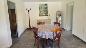 A dining area with a round table, four wooden chairs, a lace tablecloth, and a painting on the wall.