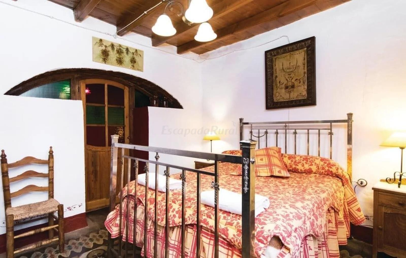 A bedroom with a bed, a wooden chair, a small table, and a wall-mounted picture.