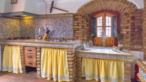 A kitchen with a stone backsplash, wooden cabinets, and yellow curtains. - Casa Rural con Encanto Coronel Cordoba Andalusia (Fuente Obejuna)