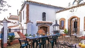 A courtyard with a dining table set for two, surrounded by chairs, a brick oven, and a small garden area with potted plants. - Casa Rural con Encanto Coronel Cordoba Andalusia (Fuente Obejuna)