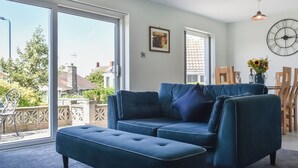 Een woonkamer met een blauwe bank, een eettafel met stoelen en een groot raam met uitzicht op buiten.