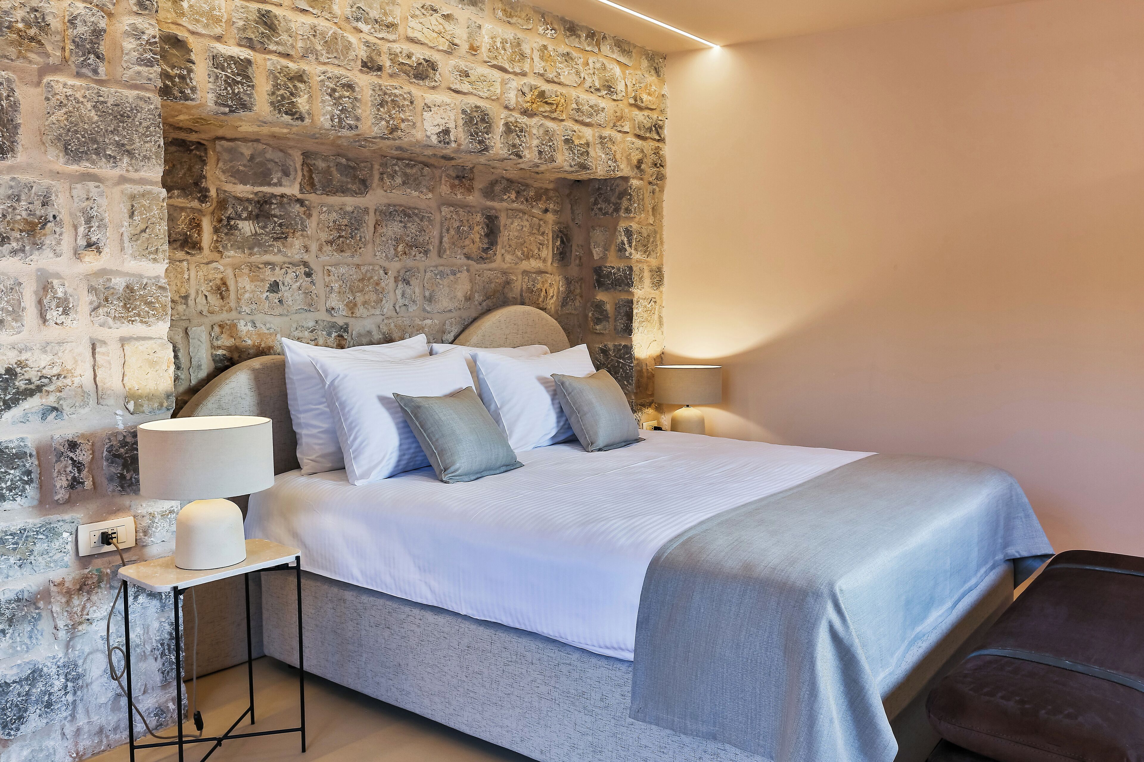 A bed with a headboard, white bedding, and a bedside table with a lamp.