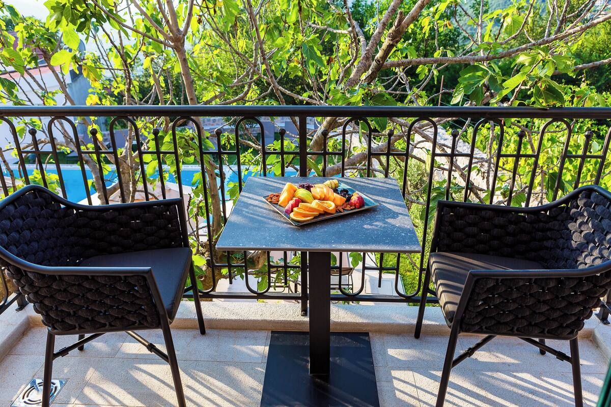 A balcony with a table set for a meal, two chairs, and a view of a pool.