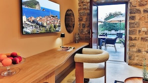 A room with a stone wall, a wooden bar area, a TV displaying a coastal town, and a view of an outdoor seating area. - Boutique hotel Ruzmarin Garden&SPA (Budva)