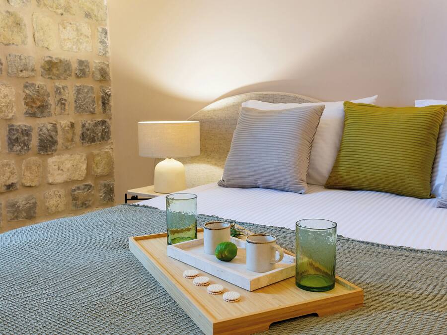 Una cama bien hecha con almohadas, una mesita de noche con una lámpara y una bandeja con vasos y una lima.
