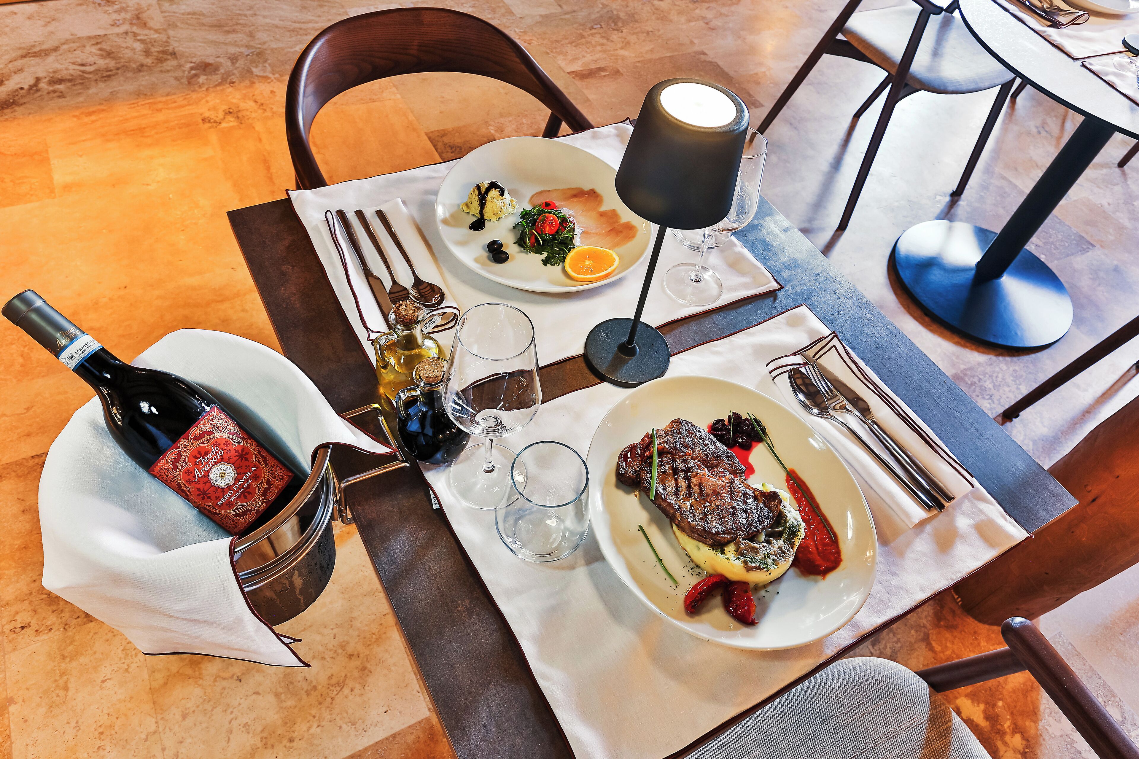 Una mesa de comedor con una botella de vino, dos platos de comida y una copa de vino.