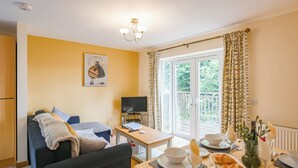 A cozy living room with a sofa, a television, and a dining area with a table set for two. - Tranquil lodge with sea views. (Plas Panteidal, near Aberdovey)