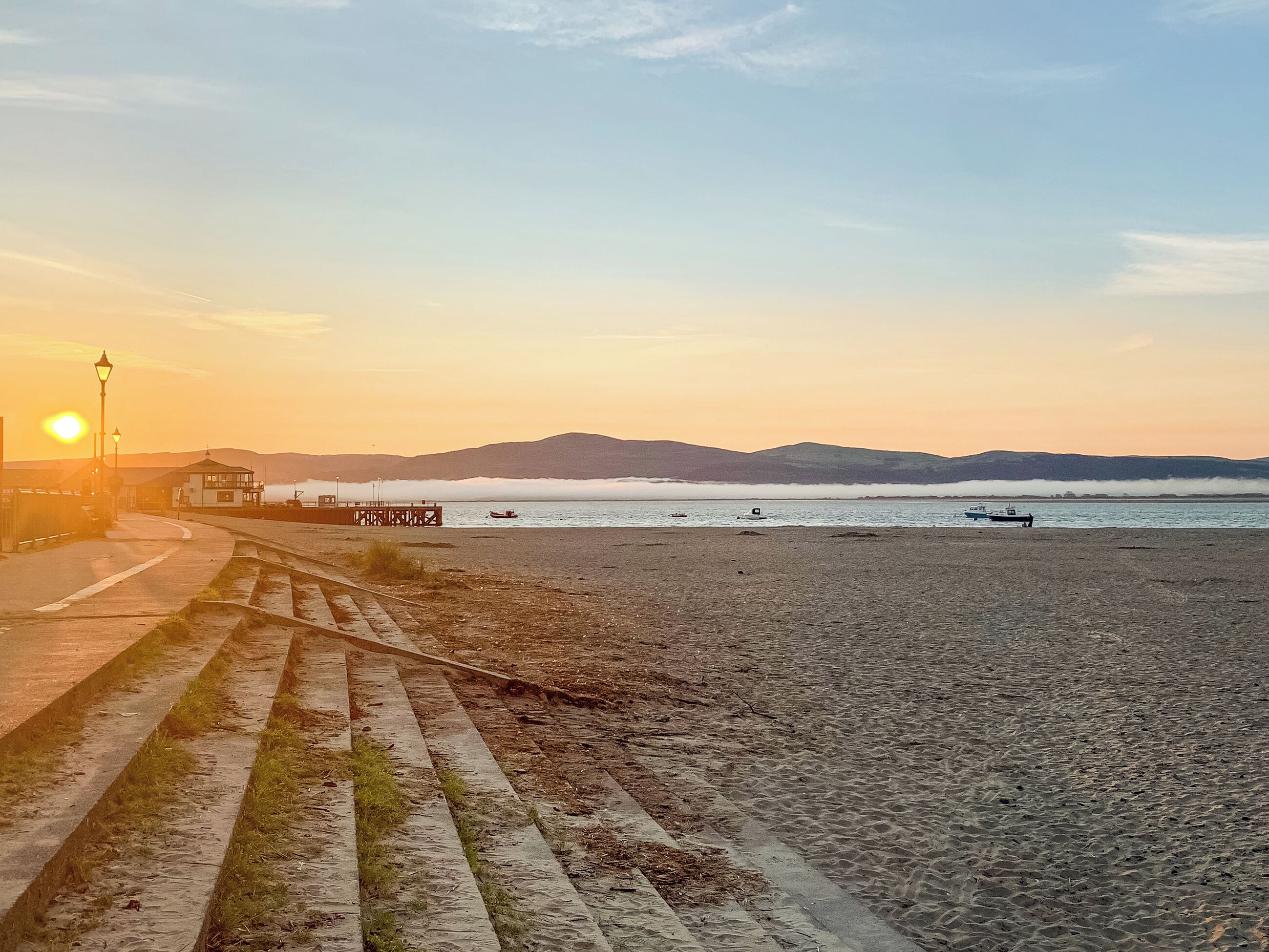 A beach with a pier, boats, and a sunset.