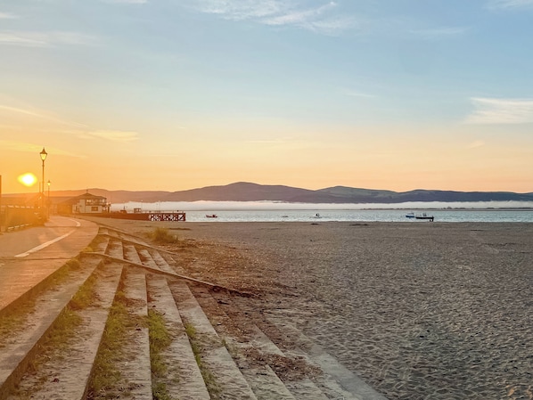 A beach with a pier, boats, and a sunset.