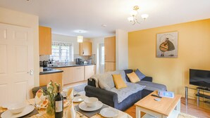 A modern living room with a sofa, a dining table set for two, and a kitchen in the background. - Tranquil lodge with sea views. (Plas Panteidal, near Aberdovey)