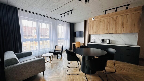 A modern living room with a sofa, a round dining table, and chairs. There is a kitchen area with wooden cabinets and a marble countertop. - Apartamenty I SORAU Old Town (Zary)
