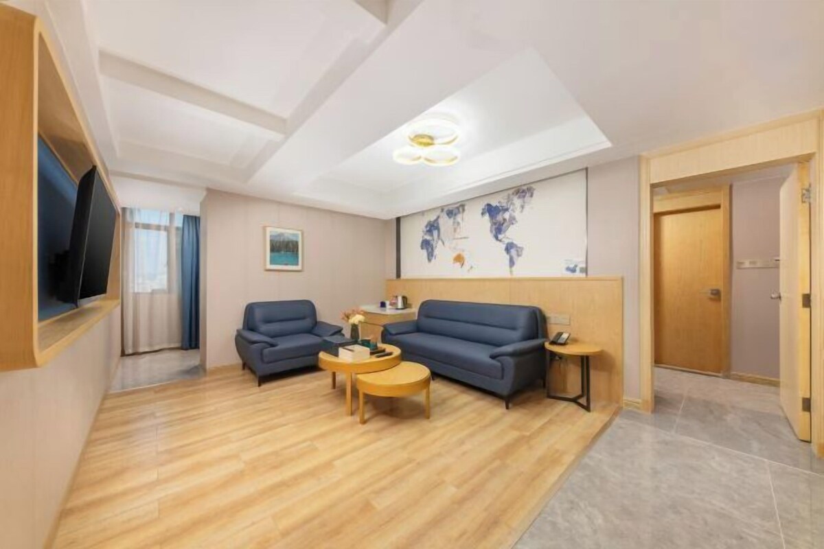 Una habitación de hotel moderna con piso de madera, dos sofás, una mesa de centro, un televisor y un mapa del mundo en la pared.