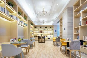 A library with bookshelves, reading tables, and chairs. - Kyriad Marvelous Hotel Dongguan Changan Light Rail Station Binhaiwan Branch (Dongguan)
